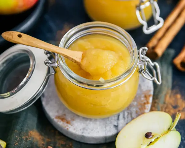 Frisch zubereitetes Apfelmus selber machen ist einfach! Ein Glas voller hausgemachtem Apfelmus, mit einem Holzlöffel und Zimtstangen.