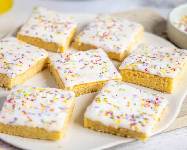 Sieben quadratische Kuchenstücke mit weißer Glasur und bunten Streuseln, perfekt für ein schnelles Fantakuchen Tassenrezept.