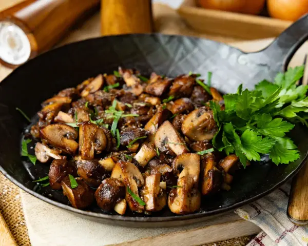Gebratene Champignons in einer Pfanne, garniert mit frischer Petersilie. Köstlich und einfach zuzubereiten.
