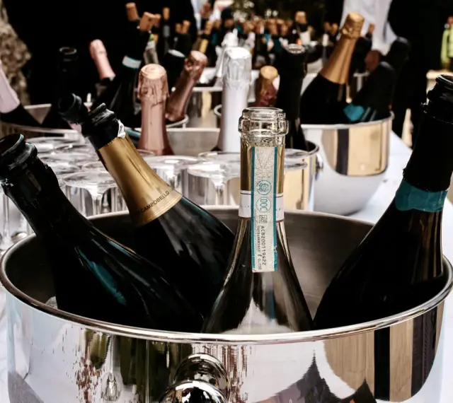 Mehrere Flaschen Sekt in einem silbernen Eiskübel, bereit für die Feier. Gläser stehen daneben.