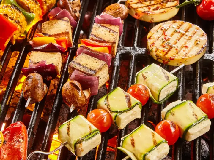 Bunte Spieße mit Tofu, Zucchini, Tomaten und Mais werden auf einem Grill zubereitet. Ein Genuss für vegetarisches Grillen!