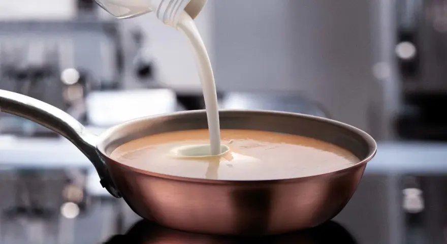 Sahne wird in eine Pfanne mit einer cremigen Sauce gegossen. Perfekt, welche Sahne zum Kochen für eine köstliche Mahlzeit.