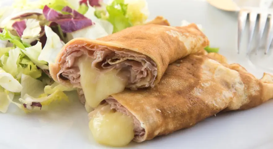Herzhafte Pfannkuchen gefüllt mit Schinken und geschmolzenem Käse, serviert mit einem frischen Salat.