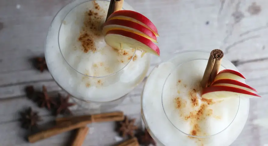 Zwei cremige Wintercocktails mit Zimt, Apfelscheiben und Sternanis.