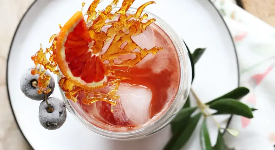 Ein erfrischender Sling Cocktail mit Blutorange, gefrorenen Beeren und Karamell-Dekoration.