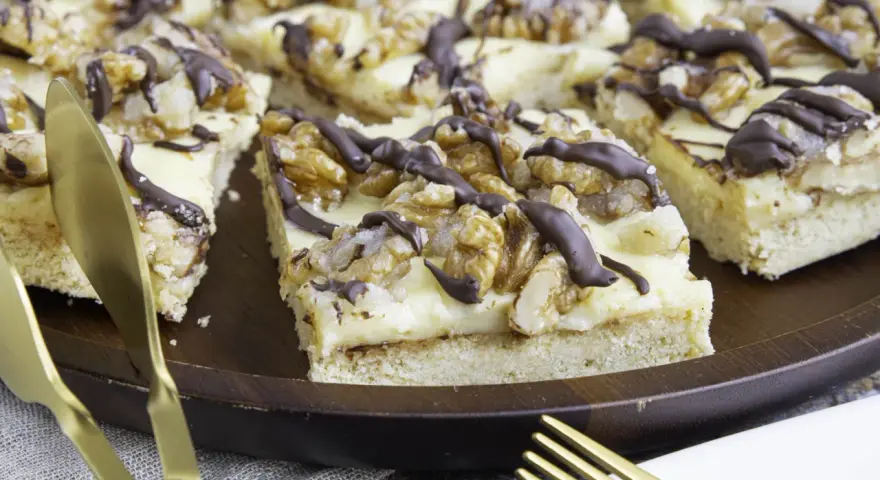 Ein "friss dich dumm kuchen" mit cremiger Füllung, Walnüssen und Schokoladendrizzle auf einem Holztablett. Goldene Gabeln liegen bereit.