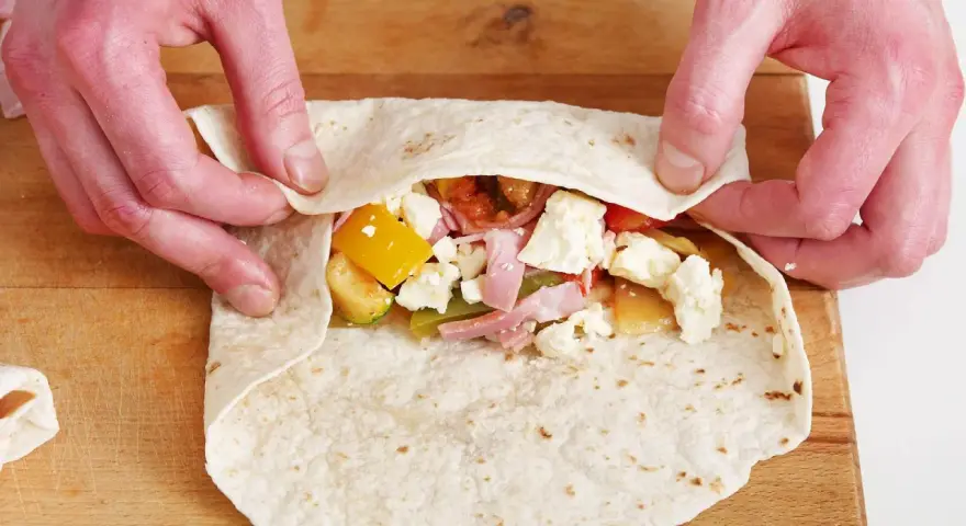 Hände falten wraps mit Gemüse, Schinken und Käse.