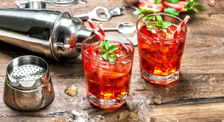 Zwei erfrischende Cocktails mit Erdbeeren und Minze, bereit zum Genießen. Dazu ein Shaker und Eiswürfel auf Holztisch. Perfekt für gute Cocktails.