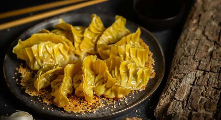 Goldbraune Gyoza auf knusprigem Sesam-Bett, bereit für ein köstliches Dumplings-Rezept. Dazu Sojasauce und Ingwer.
