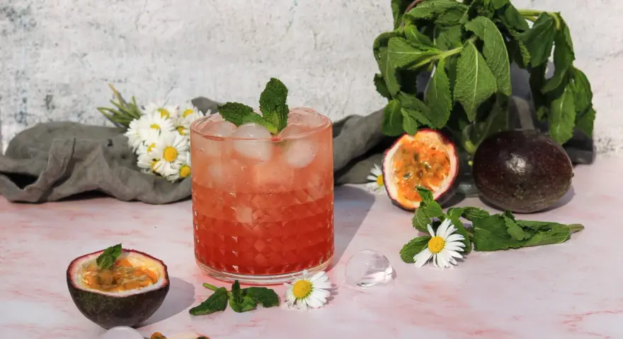 Erfrischender sanbitter cocktail mit Passionsfrucht, Minze und Eiswürfeln, garniert mit Gänseblümchen.