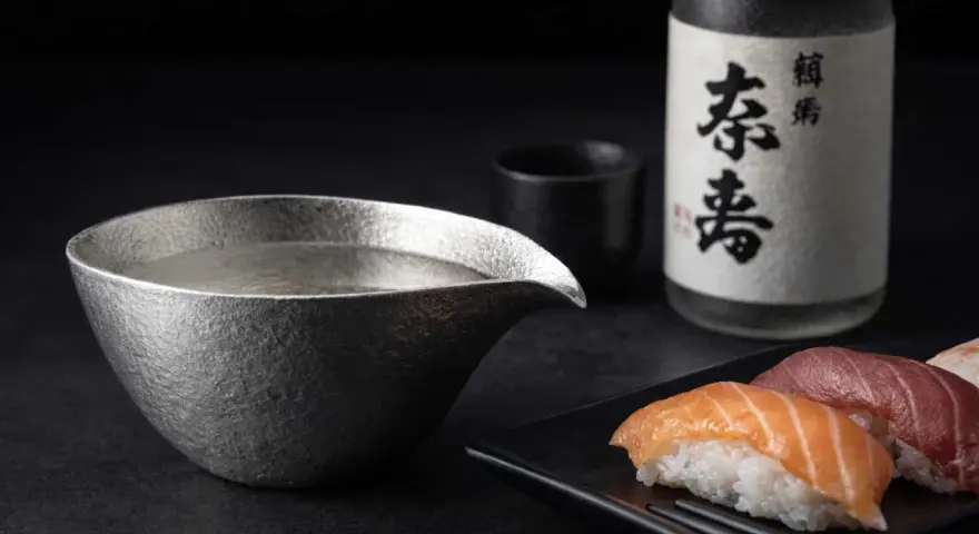 Sake-Flasche und eine Kanne mit Sake, die klassische Getränke, was trinkt man zu Sushi. Sushi-Stücke liegen daneben.