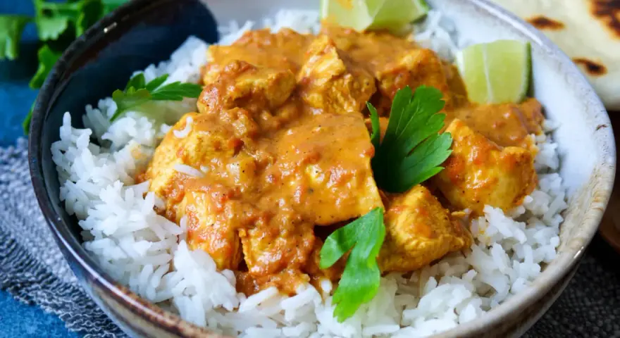 Ein köstliches indisches Curry mit zarten Hähnchenstücken in cremiger Sauce, serviert auf lockerem Reis, garniert mit frischer Petersilie und Limettenspalten.