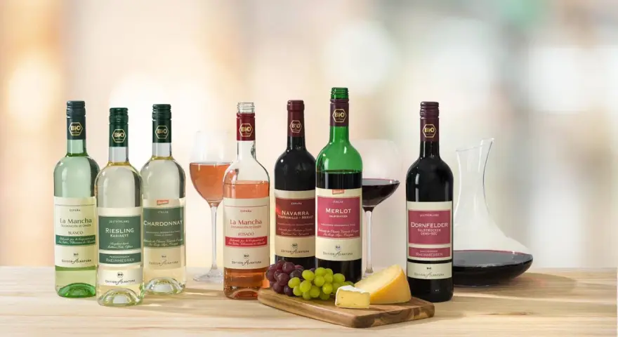Eine Auswahl an Bio-Weinen, darunter verschiedene Weißwein Sorten wie Riesling und Chardonnay, neben Rot- und Roséweinen, Käse und Trauben.