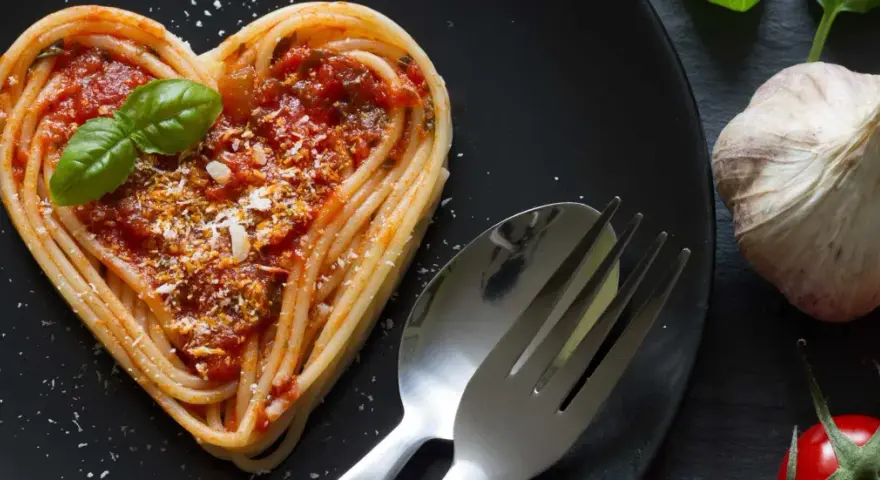 Herzförmige Spaghetti mit Tomatensoße und Basilikum, ein liebevolles Gericht für Pasta Rezepte. Daneben liegen Knoblauch und Tomaten.