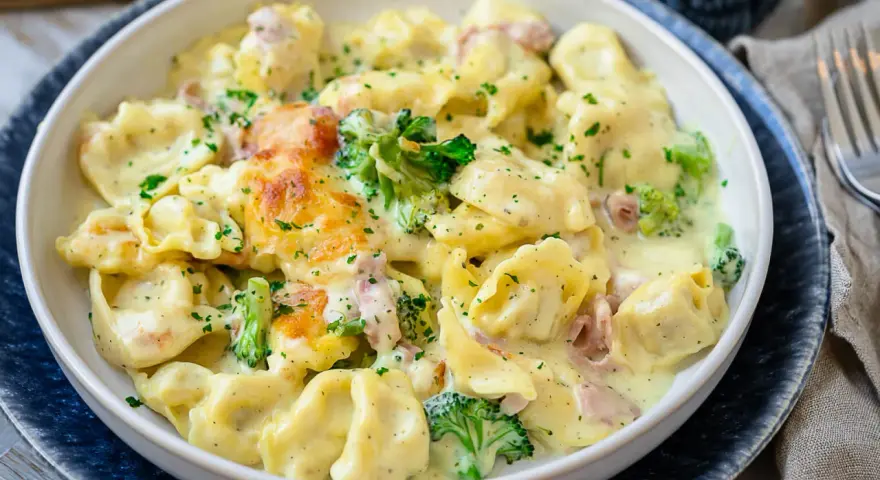 Ein cremiger Tortellini Auflauf mit Brokkoli und Schinken, überbacken mit Käse und bestreut mit Petersilie.