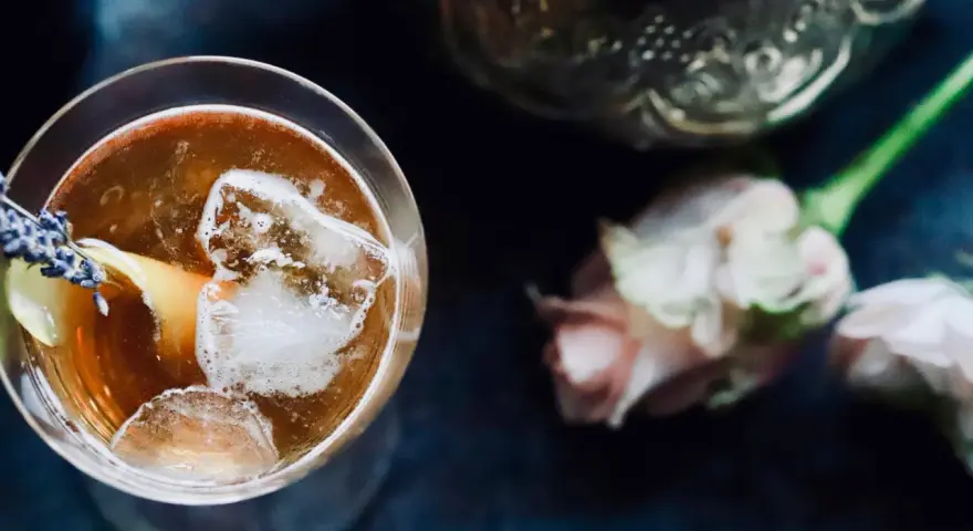 Ein erfrischender Gin Tee mit Eis, Zitrone und Lavendelblüten. Daneben zarte Rosen und eine verzierte Karaffe.