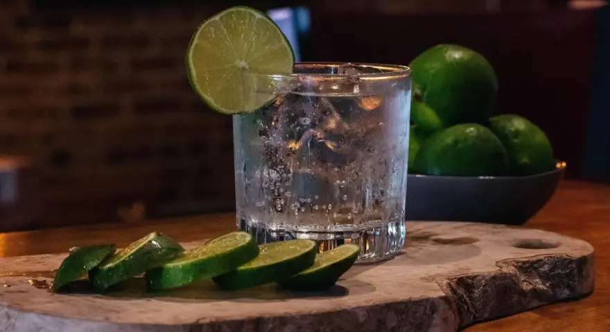 Ein erfrischender Gin Tonic, der klassische Cocktail, mit Eis, Limettenscheiben und frischen Limetten im Hintergrund.