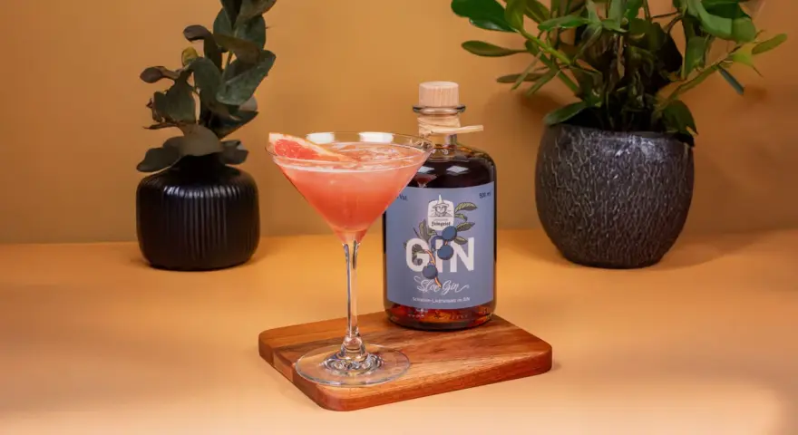 Ein erfrischender Sloe Gin Fizz mit Grapefruit-Garnitur neben einer Flasche Sloe Gin.