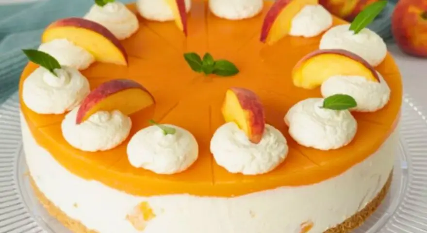 Eine Maracuja Torte mit Pfirsichstücken und Sahnetupfern, verziert mit Minze.