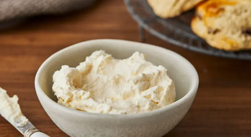 Cremiger Aufstrich in einer Schale, bereit für das perfekte Scones Rezept. Daneben ein Messer mit etwas Aufstrich.