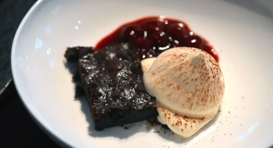 Schokoladenbrownie mit Fruchtsauce und einer perfekt hergestellten, luftigen Espuma, bestäubt mit Kakao.