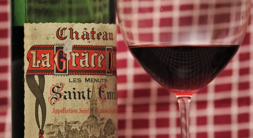 Ein Glas Rotwein neben einer Flasche Château La Grace Dieu. Die Bedeutung von "Grand Cru" auf dem Etikett deutet auf höchste Qualität hin.