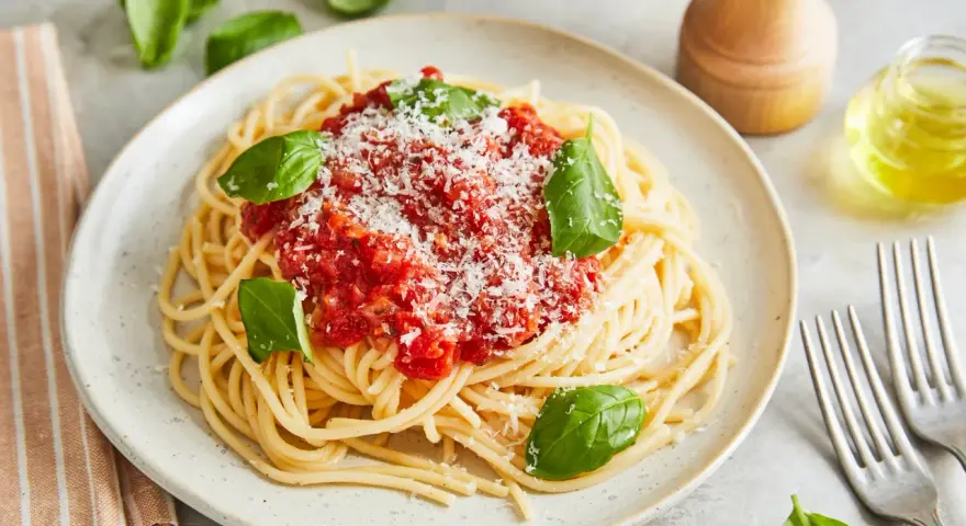 Ein Teller Spaghetti Napoli mit Tomatensauce, Parmesan und frischem Basilikum.