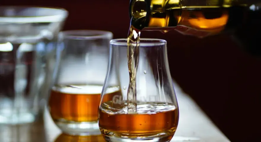 Bernsteinfarbener schottischer Whisky fließt aus einer Flasche in ein Glas. Die schottischer Whisky sorten alphabetisch zu verkosten ist ein Genuss.