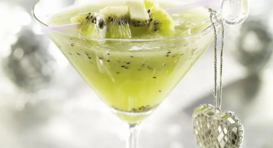 Erfrischender Kiwi-Cocktail im Martiniglas, garniert mit frischen Kiwischeiben und einem glitzernden Herz-Anhänger.