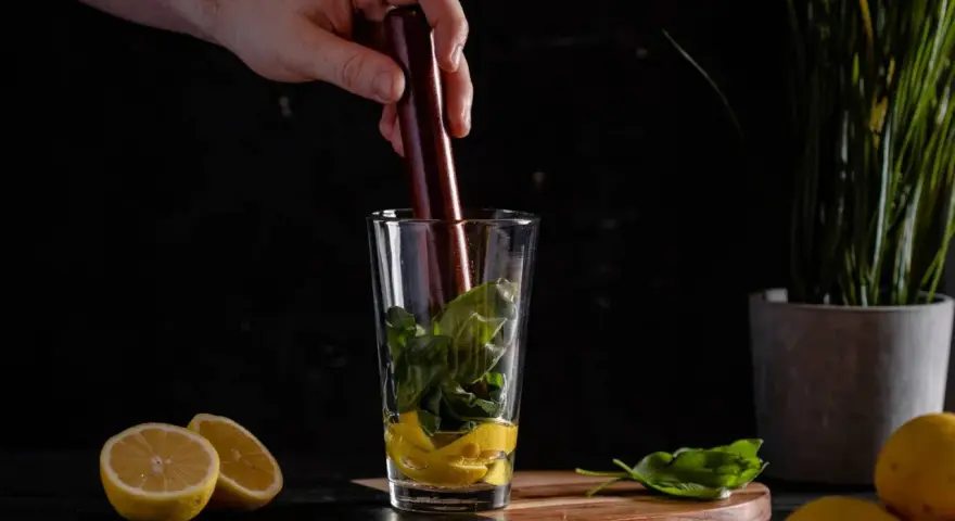 Ein Barkeeper bereitet einen erfrischenden Cocktail mit Basilikum und Gin zu, indem er die Zutaten im Glas zerdrückt.