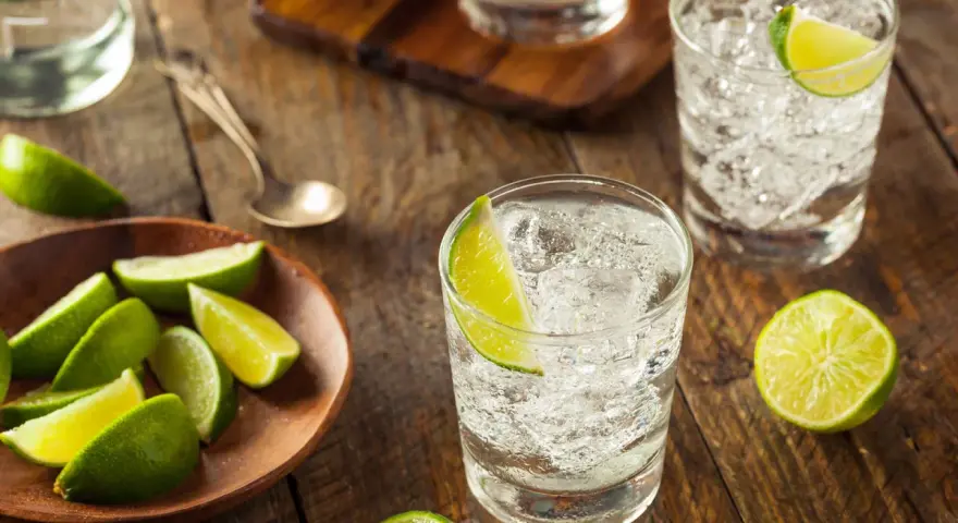 Erfrischender Jean Tonic mit Eis und Limettenspalten auf rustikalem Holztisch.