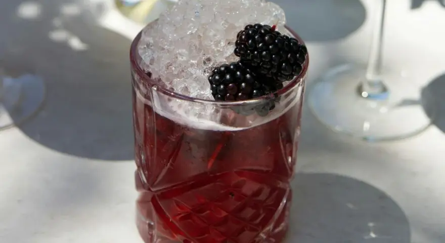 Ein Glas mit einem tiefroten Drink, gefüllt mit zerstoßenem Eis und garniert mit Brombeeren. Perfekt für die besten Cocktails an einem sonnigen Tag.