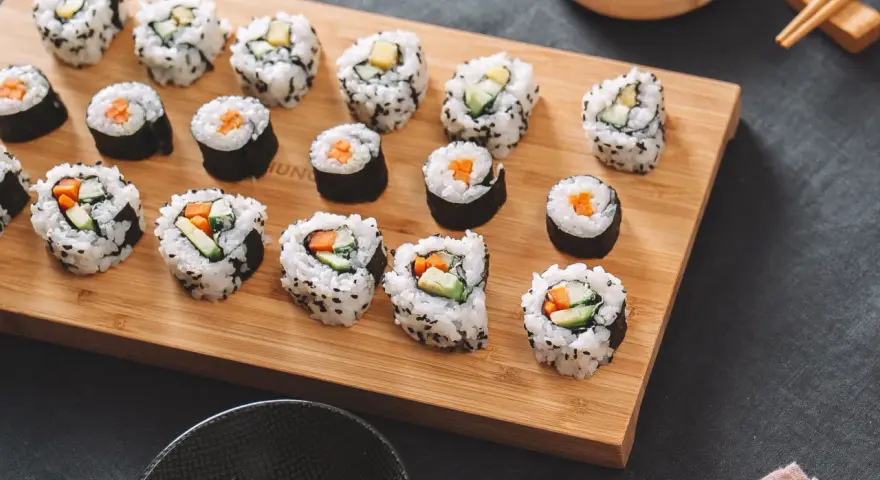 Selbstgemachtes Sushi mit Karotten und Gurken auf einem Holzbrett. So einfach kann Sushi selber machen sein!