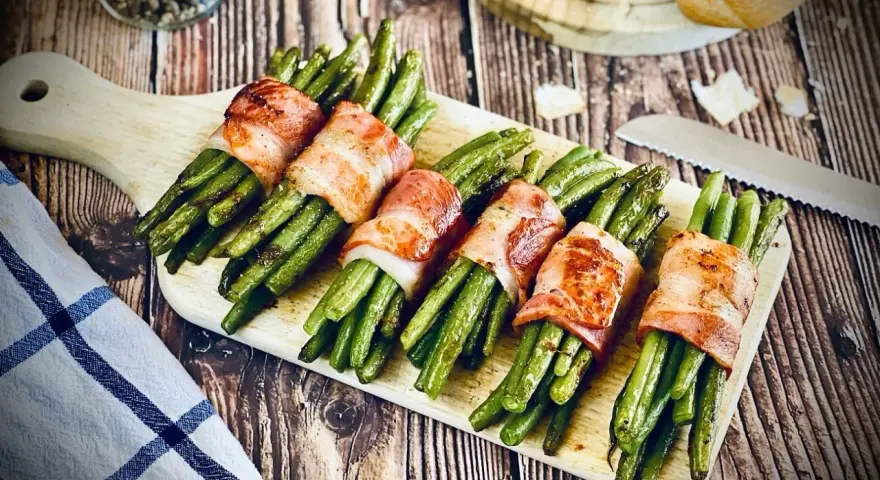Leckeres Speckbohnen Rezept: Grüne Bohnen umwickelt mit knusprigem Speck, serviert auf einem Holzbrett.
