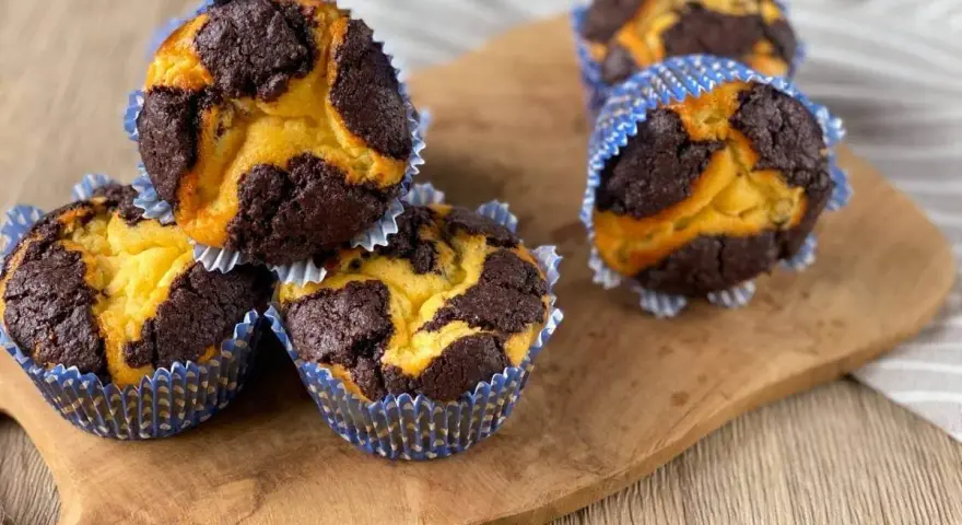 Zupfkuchen Muffins mit Marmormuster aus dunklem Schoko- und hellem Teig in blauen Papierförmchen auf einem Holzbrett.