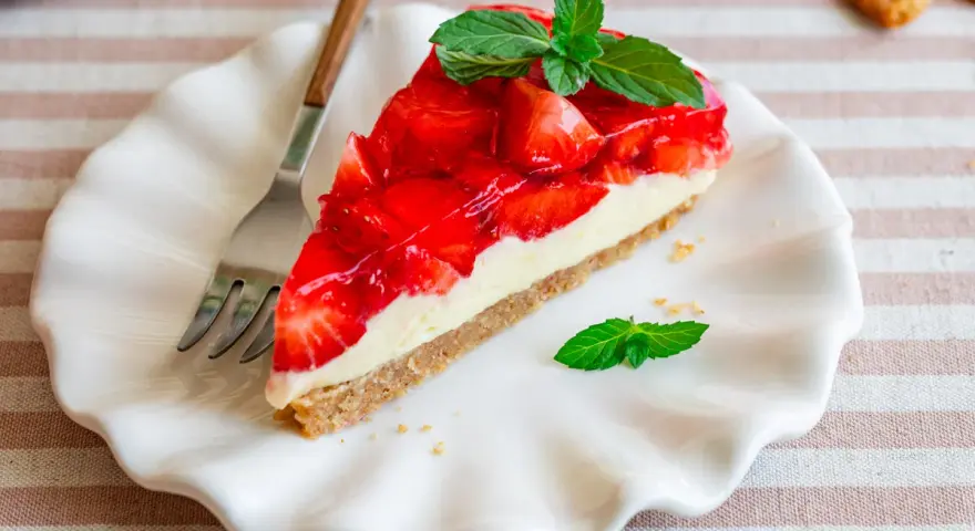 Ein Stück einfache Torte mit Erdbeeren und Minze auf einem weißen Teller.