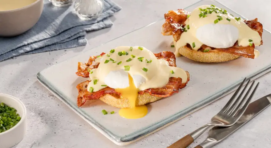 Zwei köstliche Eggs Benedict auf einem Teller, mit flüssigem Eigelb und garniert mit Schnittlauch.