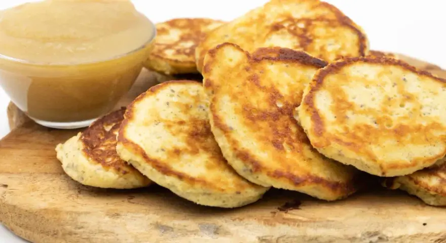 Goldbraune Quarkkeulchen ohne Kartoffeln, serviert mit Apfelmus auf einem Holzbrett.