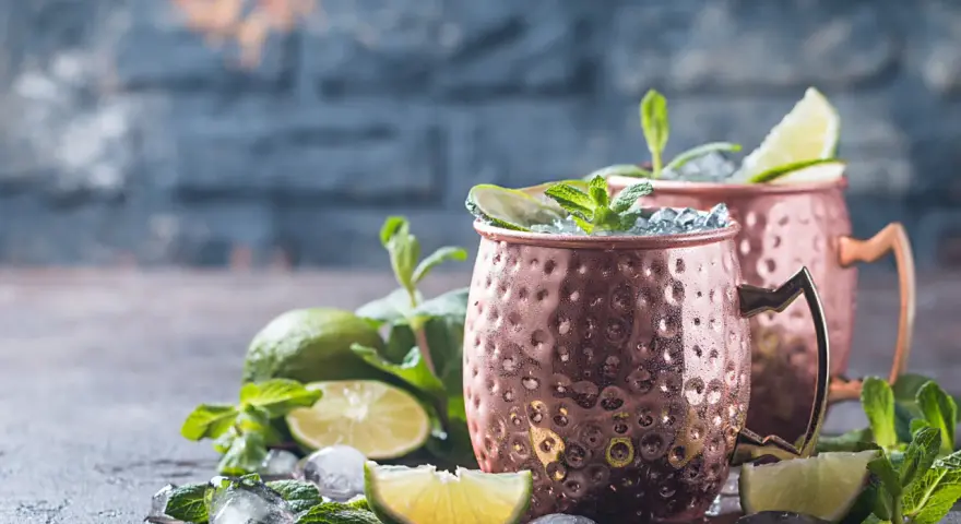 Zwei eisgekühlte Kupferbecher mit einem erfrischenden alkoholfreien Ginger Beer Cocktail, garniert mit Limette und Minze.