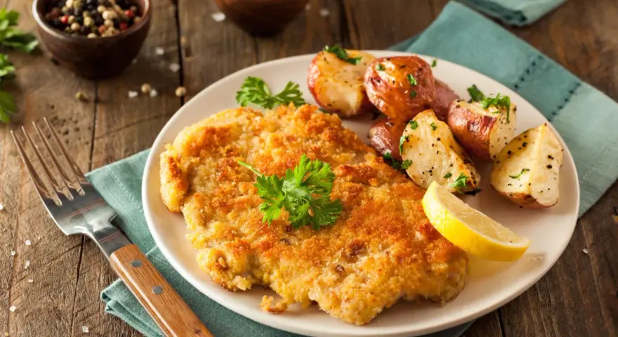 Goldbraunes Schnitzel, perfekt paniert, mit Rosmarinkartoffeln und Zitrone. Die richtige **Schnitzel panieren Reihenfolge** macht's möglich!
