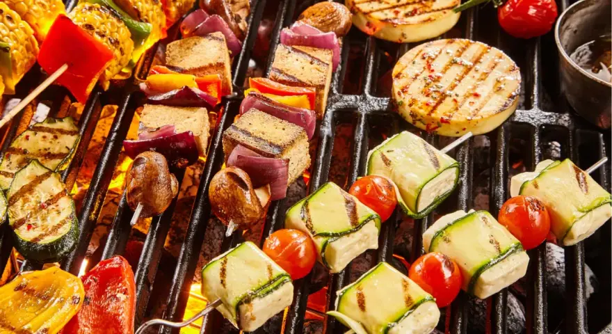 Bunte Spieße mit Tofu, Zucchini, Tomaten und Mais werden auf einem Grill zubereitet. Ein Genuss für vegetarisches Grillen!