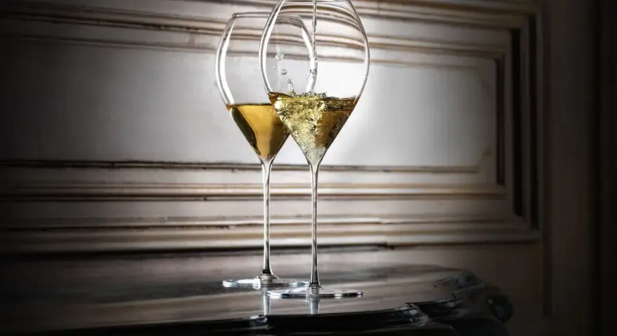 Zwei elegante Gläser, eines wird mit Champagner gefüllt. So trinkt man Champagner stilvoll.