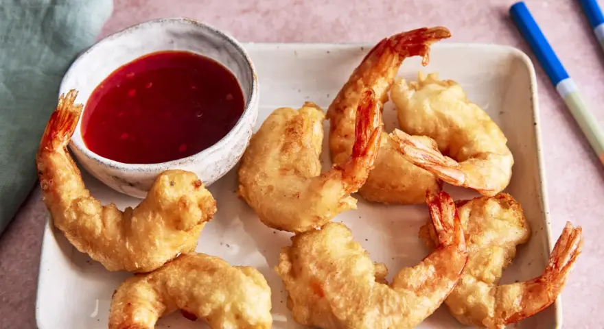 Knusprige tempura garnelen auf einem Teller mit süß-saurer Sauce und Stäbchen.