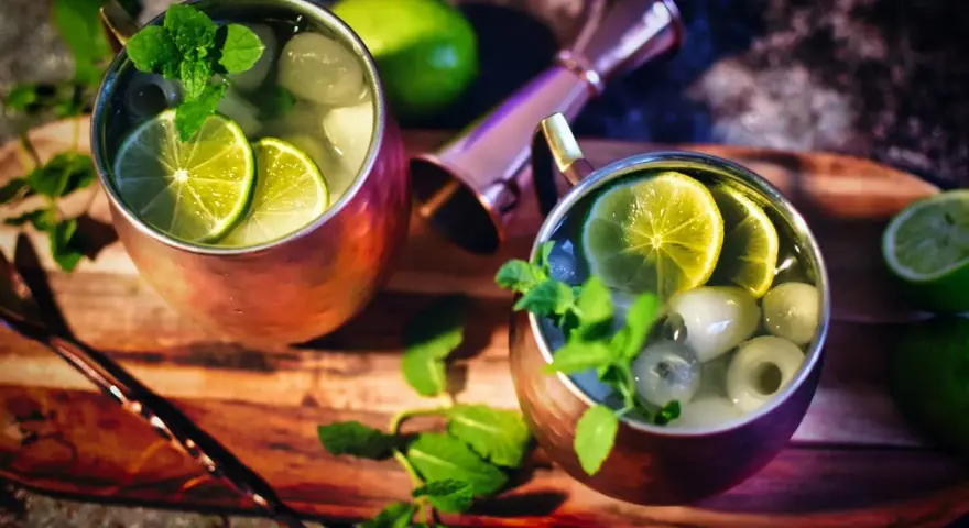 Zwei erfrischende Gin Mule Cocktails in Kupferbechern, garniert mit Limettenscheiben und Minze, bereit zum Genuss.