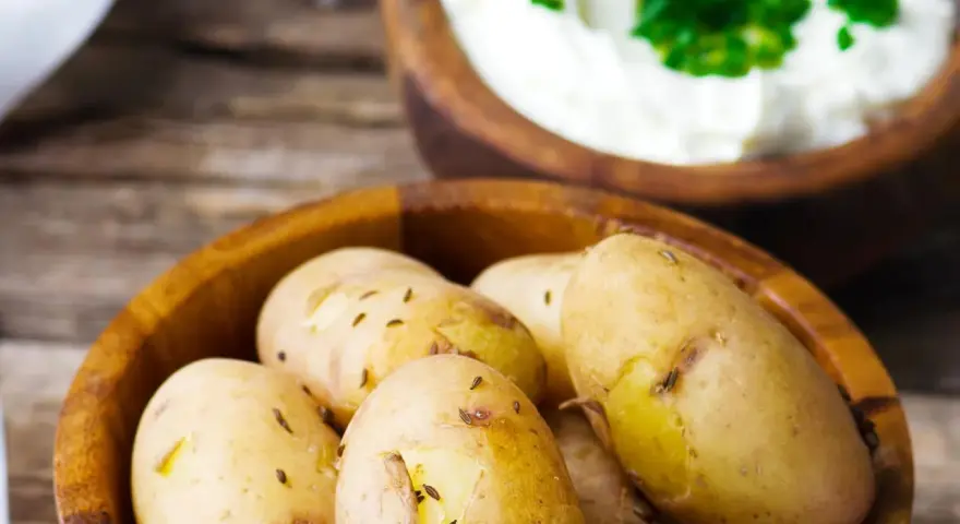 Kleine, gekochte Kartoffeln mit Kümmel in einer Holzschale, daneben eine Schale mit Quark und Kräutern. Ein rustikales Gericht: Kartoffeln mit Quark.