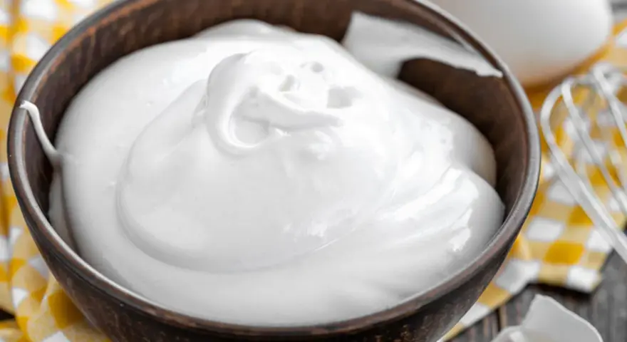 Perfekt geschlagener Eischnee in einer Schüssel, bereit für süße Kreationen. Daneben liegen Eier und ein Schneebesen.
