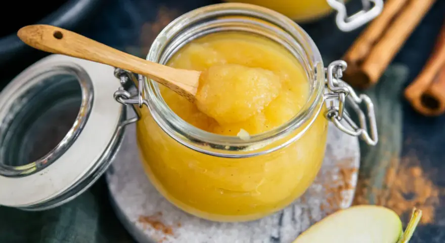 Frisch zubereitetes Apfelmus selber machen ist einfach! Ein Glas voller hausgemachtem Apfelmus, mit einem Holzlöffel und Zimtstangen.