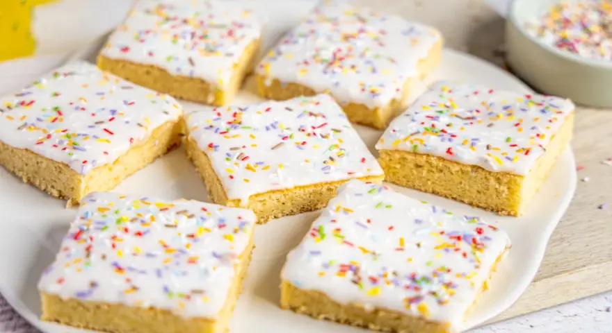 Sieben quadratische Kuchenstücke mit weißer Glasur und bunten Streuseln, perfekt für ein schnelles Fantakuchen Tassenrezept.