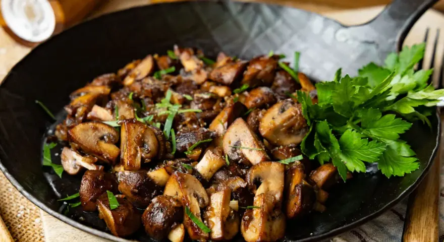 Gebratene Champignons in einer Pfanne, garniert mit frischer Petersilie. Köstlich und einfach zuzubereiten.