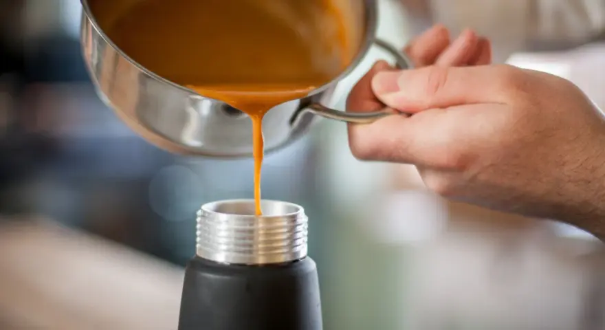 Eine orangefarbene Flüssigkeit wird aus einem Topf in ein schwarzes Gefäß gegossen. Ist das eine Espuma?